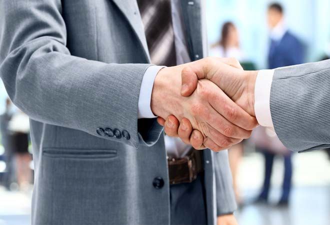 two businessmen shaking hands with other business people in the background