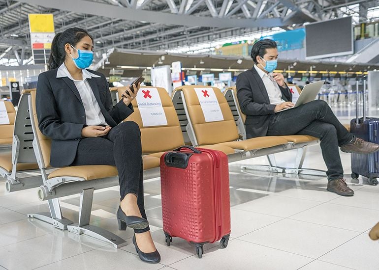 Two business people sitting in airport with masks on