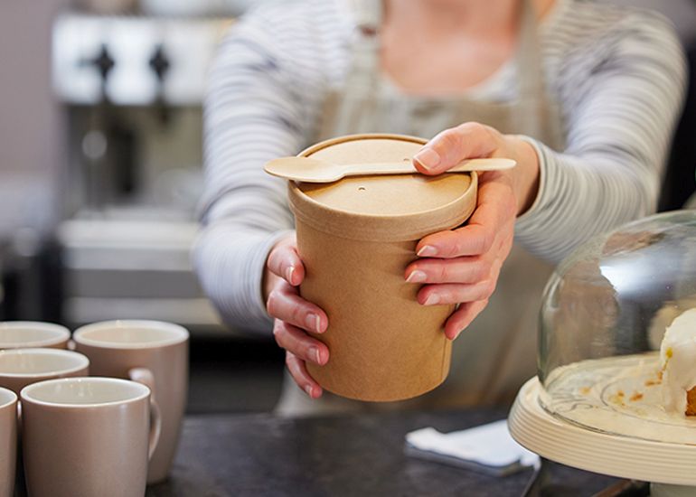 Cafe worker passing product to customer in eco-friendly packaging