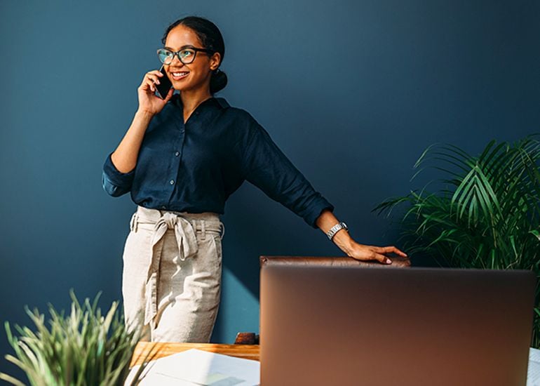 Young woman standing near desk while talking on phone