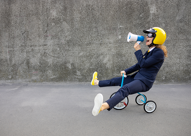 Happy business woman riding a child’s tricycle wearing a yellow helmet