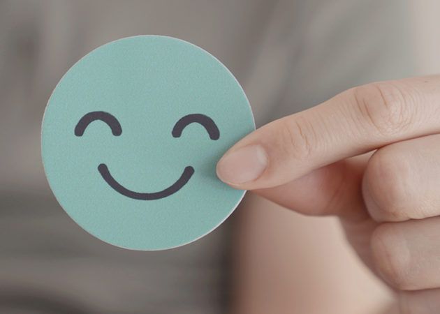Hand holding a blue cardboard circle with a smily face drawn on