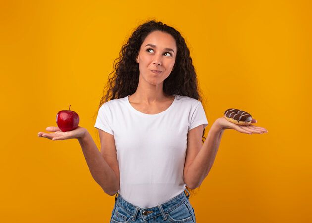 Woman deciding between healthy apple or unhealthy donut