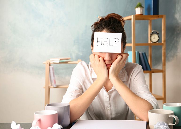 Stressed woman at desk with 'help' sign on her forehead