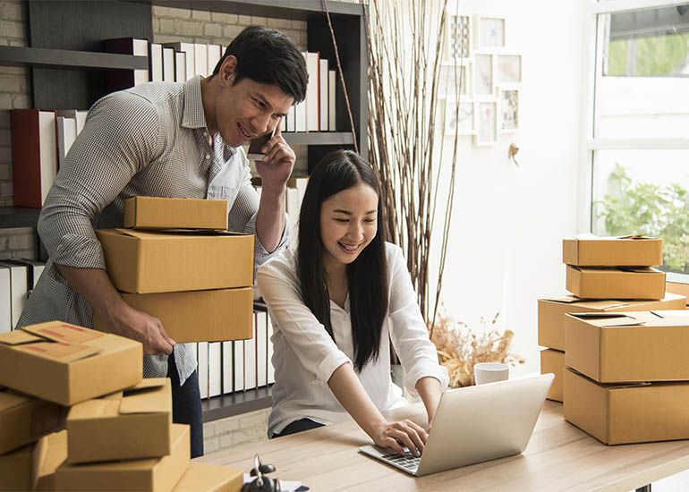 Couple packing boxes and checking online orders on laptop