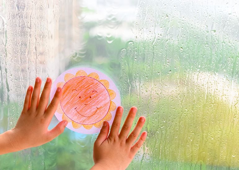 child's hands sticking a sunshine drawing onto a rainy window pane