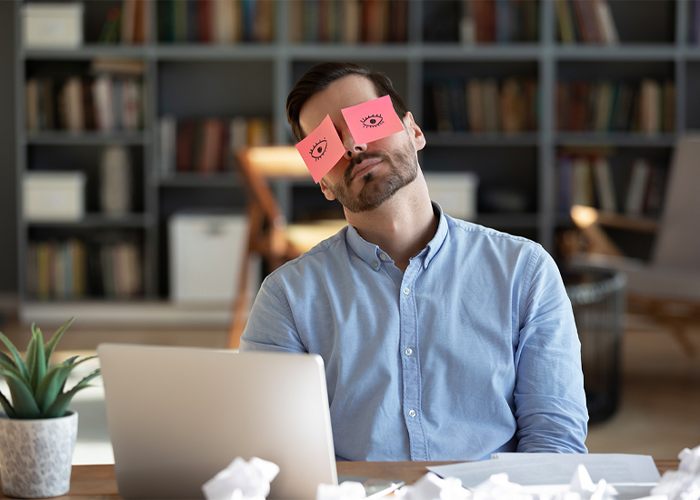 Tired man at desk with post-it notes with eyes stuck on his own eyes