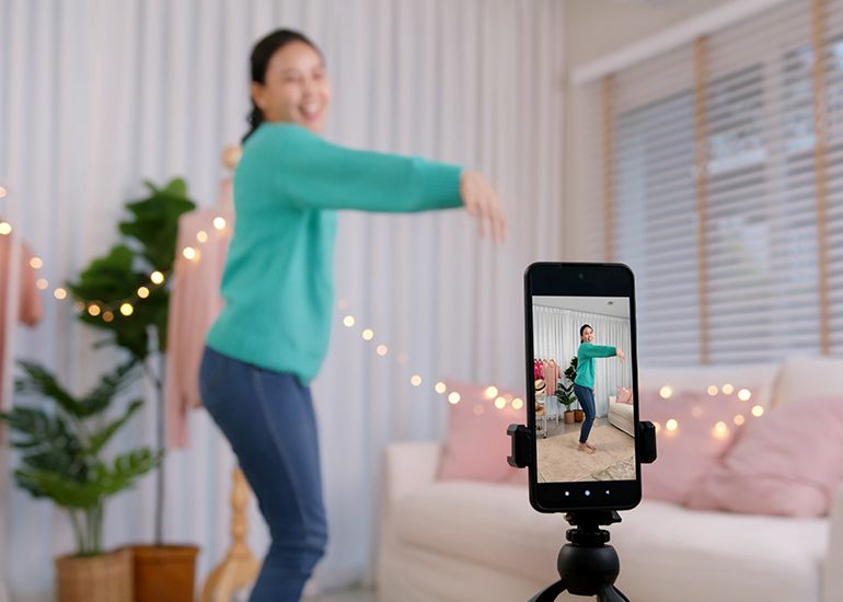 Young woman dancing in front of smartphone on camera stand
