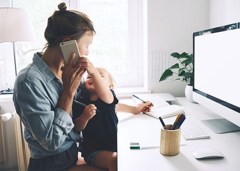 Mother at home work desk with phone to ear and toddler on her lap