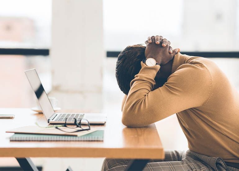 tired, exhausted person sitting at desk with head in hands