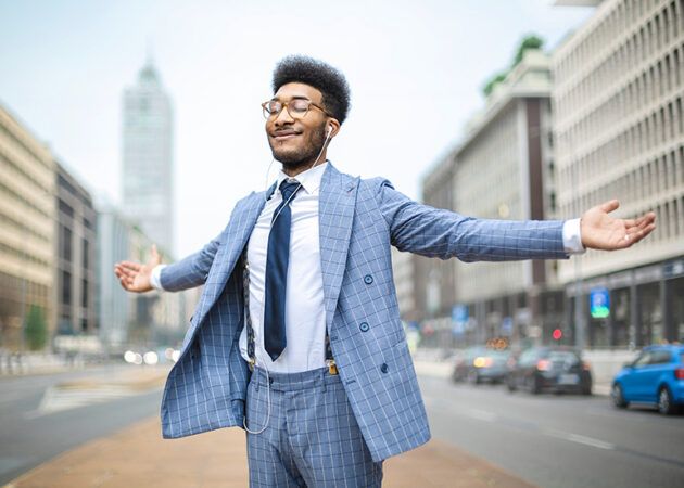 Smiling young businessman standing in street with arms wide