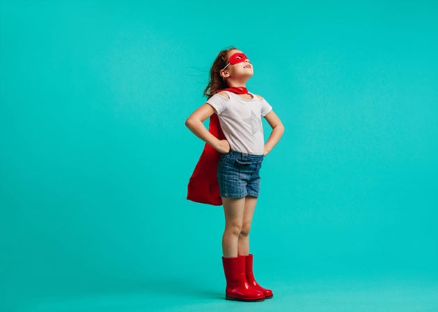 Confident little girl in cape, eye mask, and gumboots