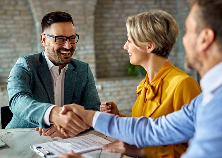 Three people at a desk, shaking hands and signing a contract