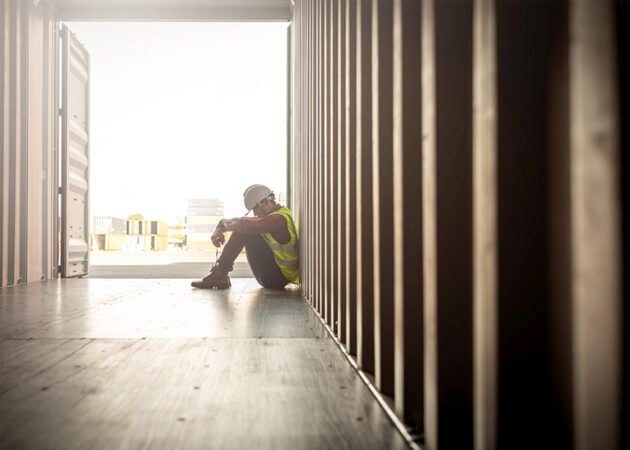 Tired, stressed worker sitting with hard hat on and head down