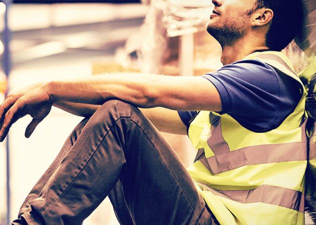 Tired factory worker sitting against pallet