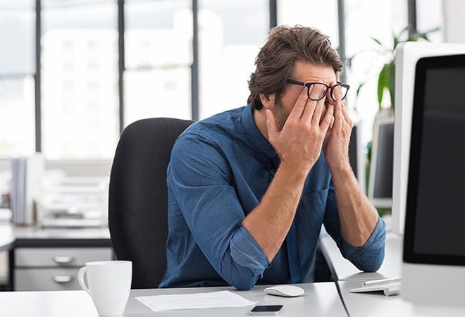 man rubbing eyes in front of computer