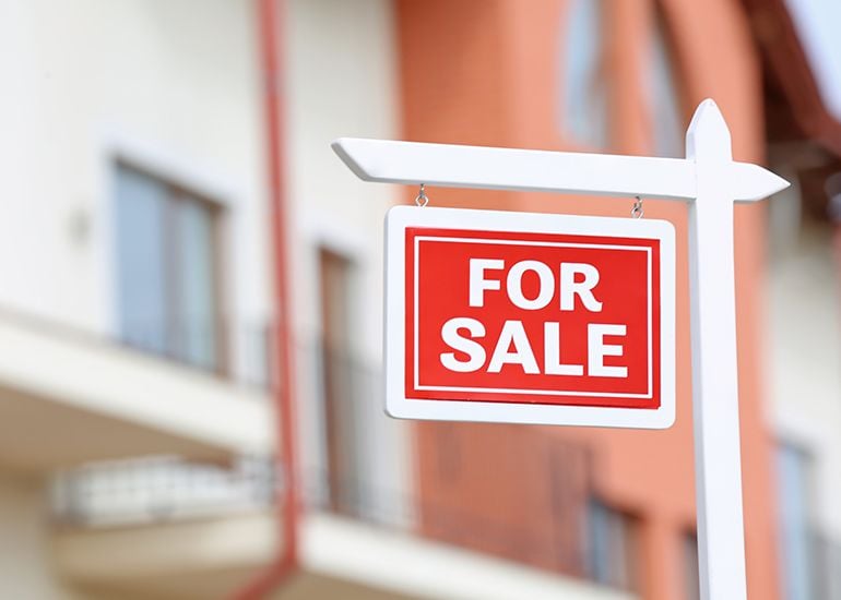 Red for sale sign in front of buildings