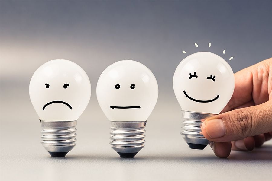 three lightbulbs with sad, neutral and happy faces drawn on