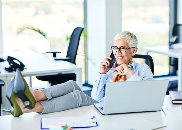 Mature business woman chatting on phone with feet up on desk
