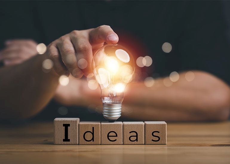 Man holding lightbulb over wooden blocks which read 'ideas'