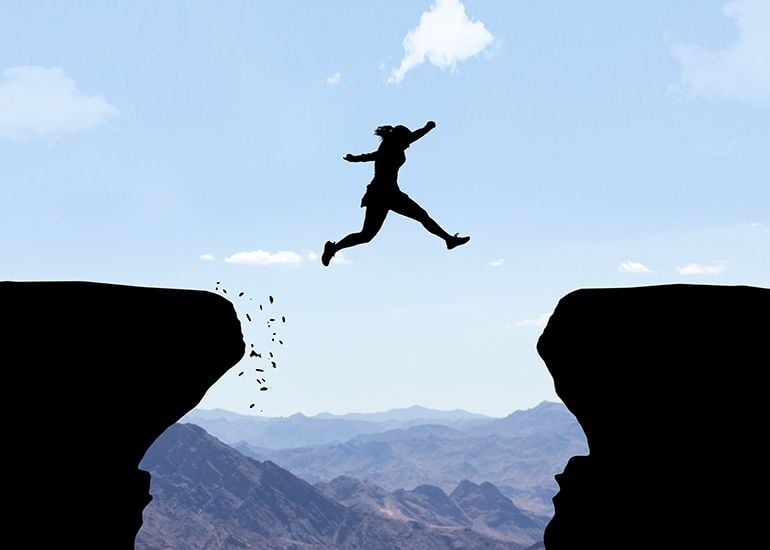 woman jumping between two cliffs on mountain top
