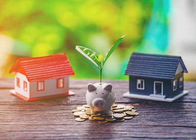 Piggy bank sitting on pile of coins between two houses