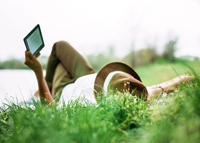 person lying on grass reading from an e-reader