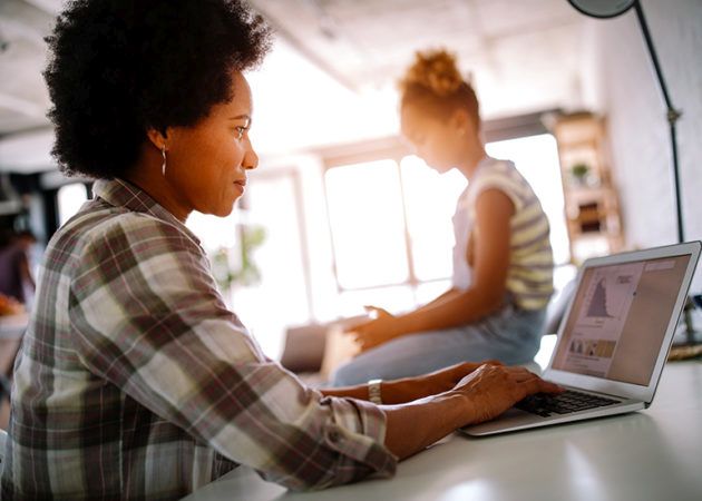 Mother working at kitchen bench with child in background