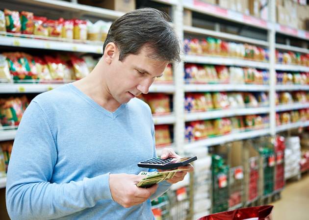 A male consumer in a supermarket looks at a calculator as he checks his money.